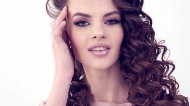 Uzun kıvırcık saçlı, gülümseyen güzel bir kadın. Güzel surat. Moda modeli. Moda makyajı. Göz makyajlı çekici seksi bir kız. Bir kadının yakın çekim yüzü. Yavaş çekim 4k görüntü.   