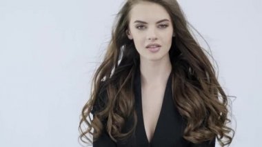 Kıvırcık uzun kahverengi saçlı güzel bir kadının 4K görüntüsü. Moda modeli kameraya bakıyor. Kafkasyalı bir kızın çarpıcı yüzü. Güzel gözleri olan seksi bir manken. Ağır çekim. Güzellik konsepti 