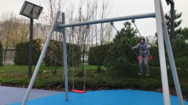 Salıncakta sallanan neşeli Avrupalı çocuk. Neşeli bir çocuk parkta salıncakta sallanıyor. Sokakta salıncakta sallanan mutlu çocuk. Sonbahar sezonu. Bulutlu hava.  