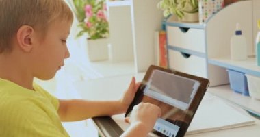 Evde tabletli bir öğrenci. Çocuk ekran tabletine bakıyor. Beyaz çocuk elinde tablet ve daktilo metni tutuyor. Çocuk internette vakit geçirir. Gerçek zamanlı.. 