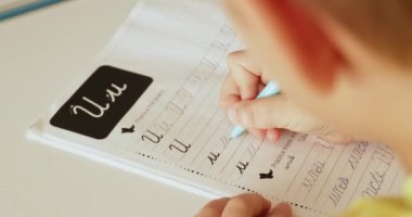 Mektupları okul defterine yazan çocuk. Öğrenci evde el yazısıyla ödev yapıyor. Mektupları okul çocuğu yazıyor. Çocuk okuldan sonra ev ödevi yapar. Gerçek zamanlı. 4k görüntü     