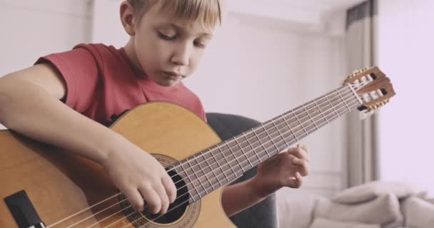 ギターを持った少年 8歳の少年がクラシックギターを弾く 白人の子供はギターを弾くことを学ぶ リアルタイムだ中に入って自然光よ低角度表示 — ストック動画