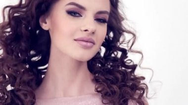 Uzun kıvırcık saçlı, gülümseyen güzel bir kadın. Güzel surat. Moda modeli. Moda makyajı. Göz makyajlı çekici seksi bir kız. Bir kadının yakın çekim yüzü. Yavaş çekim 4k görüntü.   