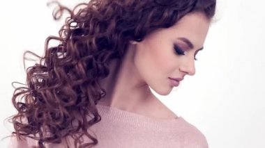 Uzun kıvırcık saçlı güzel bir kadın. Güzel surat. Moda modeli. Moda makyajı. Göz makyajlı çekici bir kız. Bir kızın yakın çekim yüzü. Yavaş çekim 4K görüntüsü. Seksi esmer bayan..  
