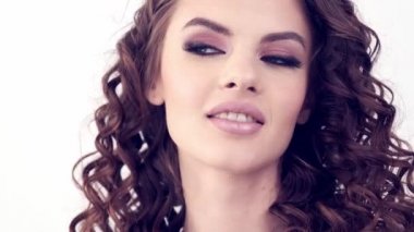 Uzun kıvırcık saçlı, gülümseyen güzel bir kadın. Güzel surat. Moda modeli. Moda makyajı. Göz makyajlı çekici seksi bir kız. Bir kadının yakın çekim yüzü. Yavaş çekim 4k görüntü.   