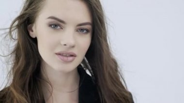 Kıvırcık uzun kahverengi saçlı güzel bir kadının 4K görüntüsü. Moda modeli kameraya bakıyor. Kafkasyalı bir kızın çarpıcı yüzü. Güzel gözleri olan seksi bir manken. Ağır çekim. Güzellik konsepti 