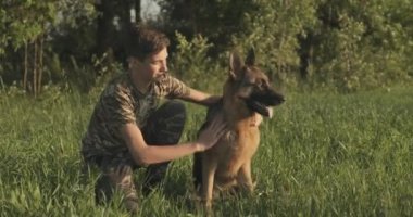Doğada köpeği olan bir genç. 15 yaşında köpek besleyen bir çocuk Alman çoban köpeği besliyor. Sahada köpekle gülümseyen mutlu bir genç. Beyaz adam çayırda evcil hayvanıyla oynuyor. Gerçek zamanlı..