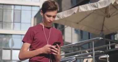 Parkta cep telefonu kullanan bir genç. Açık havada cep telefonu kullanan gülümseyen genç bir adam. Cep telefonu olan mutlu bir çocuk. Şehir manzarası. Yakışıklı adam akıllı telefon kullanıyor. 4 bin. Gerçek zamanlı..