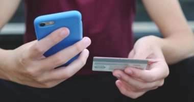 İnsanlar açık havada, kredi kartı ve cep telefonu kullanarak online alım yapıyorlar. İnsan eli cep telefonunu banka kartıyla tutuyor. Erkek eller online alışveriş için akıllı telefon ve kredi kartı kullanır. Yakın çekim..