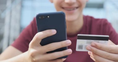İnsanlar açık havada, kredi kartı ve cep telefonu kullanarak online alım yapıyorlar. İnsan eli cep telefonunu banka kartıyla tutuyor. Erkek eller online alışveriş için akıllı telefon ve kredi kartı kullanır. Yakın çekim..