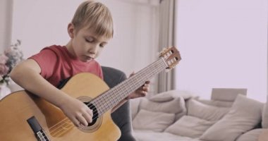 Gitarlı genç bir çocuk. 8 yaşındaki çocuk klasik gitar çalıyor. Kafkas çocuk gitar çalmayı öğreniyor. Gerçek zamanlı. Yakınlaştır. Doğal ışıklandırma. 