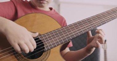 Gitarlı genç bir çocuk. 8 yaşındaki çocuk klasik gitar çalıyor. Kafkas çocuk gitar çalmayı öğreniyor. Gerçek zamanlı. Yakınlaştır. Doğal ışıklandırma. Düşük açı görünümü.