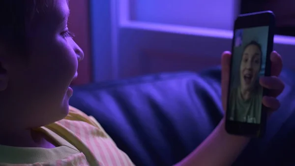 笑着的男孩看着屏幕上的智能手机，用他的手机说话 图库照片