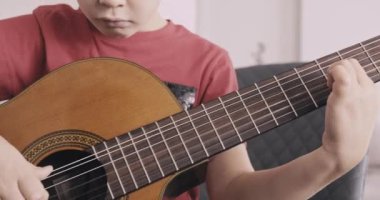 Gitarlı genç bir çocuk. 8 yaşındaki çocuk klasik gitar çalıyor. Kafkas çocuk gitar çalmayı öğreniyor. Gerçek zamanlı. Yakınlaştır. Doğal ışıklandırma. Düşük açı görünümü.