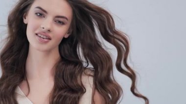 Uzun kıvırcık kahverengi saçlı, gülümseyen güzel bir kadın. Moda modeli stüdyodaki kameraya bakıyor. Çekici esmer bir kadının yakın çekim yüzü. Seksi görünüşlü seksi bir manken. 4K görüntü. Yavaş çekim. 