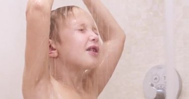 Duştaki küçük çocuk. Kafkasyalı çocuk banyoda duş alıyor. İyileştirici çocuk sıcak su akıntısı altında yıkanır. 8 yaşındaki Avrupalı çocuk saçlarını suyla yıkıyor. Gerçek zamanlı. Düşük açı. 