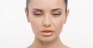 Yüzü temiz genç bir kadının yakından çekilmiş yüzü. Cilt bakımı. Seksi bakışlı güzel kız kameraya dönüyor. Güzel, sağlıklı bir kadın. Taze bir yüz ve beyaz bir arka plan. Yavaş çekim