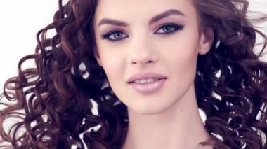 Uzun kıvırcık saçlı güzel bir kadın. Güzel surat. Moda modeli. Moda makyajı. Göz makyajlı çekici bir kız. Bir kızın yakın çekim yüzü. Yavaş çekim 4K görüntüsü. Seksi esmer bayan..  