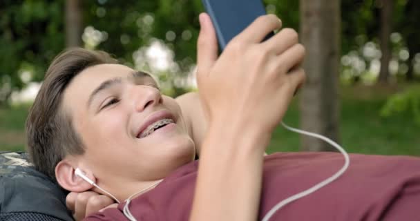 Портрет Счастливого Подростка Мобильным Телефоном Лежащим Скамейке Парке Улыбающийся Молодой — стоковое видео