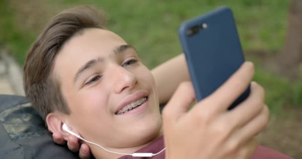 Portrait Happy Teenage Boy Mobile Phone Lying Bench Park Smiling — Wideo stockowe