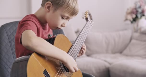 一个拿着吉他的小男孩 8岁的男孩弹古典吉他 这个高加索小孩学会了弹吉他 放大放大 自然光 — 图库视频影像