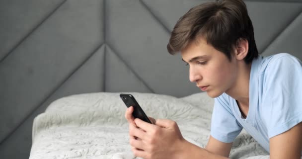 青少年们在家里用智能手机玩游戏 英俊的男孩正在沙发上用手机打发时间 游戏玩家在手机上玩 生活方式的概念 实时录像 — 图库视频影像