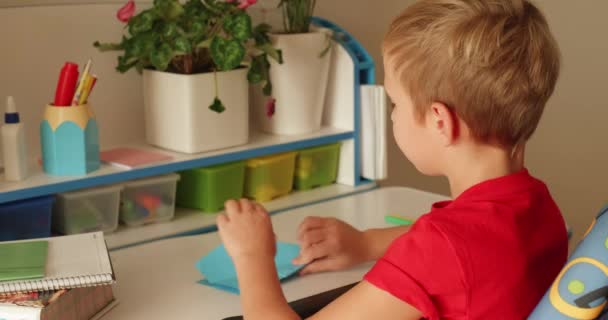 8歳の男の子は紙から飛行機を作り それを起動します 家庭での子供の余暇時間 賢い少年が飛行機を設計する 白人の少年は紙からおもちゃを作っている リアルタイム — ストック動画