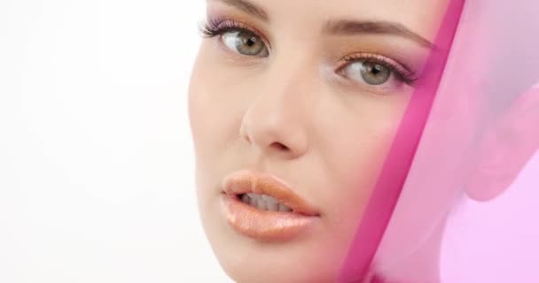 Nahaufnahme Gesicht eines Modells mit hellem Make-up. Frau versteckt sich hinter farbigem, transparentem Plastikteil. weibliches Gesicht mit orangefarbenem Make-up. modische Mädchen. sexy Mädchen schaut aus dem lila Ding