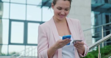 Yetişkin bir kadın kredi kartı ve cep telefonu kullanarak online alışveriş yapıyor. Gülümseyen iş kadını, açık havada, banka kartlı cep telefonuyla online alışveriş yapıyor. Bayan akıllı telefon ve kredi kartı kullanıyor.