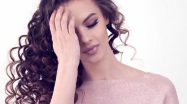Uzun kıvırcık saçlı güzel bir kadın. Güzel surat. Moda modeli. Moda makyajı. Göz makyajlı çekici bir kız. Bir kızın yakın çekim yüzü. Yavaş çekim 4K görüntüsü. Seksi esmer bayan..  