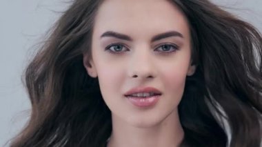 Uzun kıvırcık kahverengi saçlı güzel bir kadın. Moda modeli stüdyodaki kameraya bakıyor. Çekici esmer bir kadının yakın çekim yüzü. Saexy görünüşlü seksi bir manken. 4K görüntü. Yavaş çekim. 