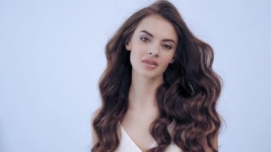 Uzun kıvırcık kahverengi saçlı güzel bir kadın. Moda modeli stüdyodaki kameraya bakıyor. Çekici esmer bir kadının yakın çekim yüzü. Saexy görünüşlü seksi bir manken. 4K görüntü. Yavaş çekim. 