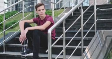 Ergen kulaklıkla müzik dinliyor. Kendine güvenen genç yakışıklı adam açık havada, kulaklıkla müzik dinliyor. Kulaklıklı güzel bir gencin portresi. Şehir manzarası. 4 bin. Gerçek zamanlı..  