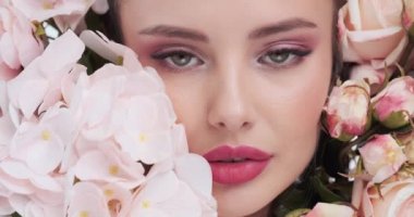 Face with flowers. Beautiful caucasian woman with fresh skin. Closeup female face with flowers. Beauty concept. Skin care. Young girl with natural makeup. 4k. Slow motion
