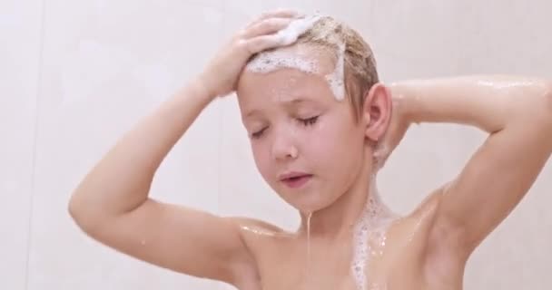 小さな男の子はシャワーでシャンプーで髪を石鹸ます 子供は暖かい水の流れの下で洗う 白人の子供は浴室でシャワーを浴びます ヨーロッパの少年は髪を水ですすいでいる スローモーション — ストック動画