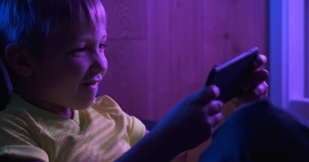 兴奋的男孩在晚上玩游戏 游戏玩家在游戏中使用智能手机 小高加索小孩拿着手机玩网络游戏 快乐的孩子会花时间在网上 — 图库视频影像