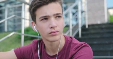 Ergen kulaklıkla müzik dinliyor. Kendine güvenen genç yakışıklı adam açık havada, kulaklıkla müzik dinliyor. Kulaklıklı güzel bir gencin portresi. Şehir manzarası. 4 bin. Gerçek zamanlı..  