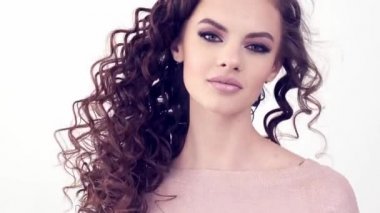 Uzun kıvırcık saçlı güzel bir kadın. Güzel surat. Moda modeli. Moda makyajı. Göz makyajlı çekici bir kız. Bir kızın yakın çekim yüzü. Yavaş çekim 4K görüntüsü. Seksi esmer bayan..  