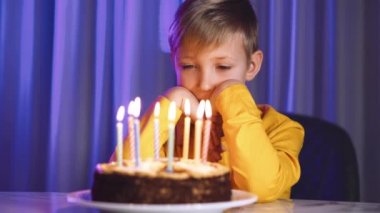 Üzgün çocuk doğum gününde mum yakan pastaya bakar. Doğum gününde üzgün bir beyaz çocuk. Yalnız çocuk elinde mumlarla pastanın önünde oturuyor. Mutsuz beyaz çocuk doğum günü pastasına bakıyor..