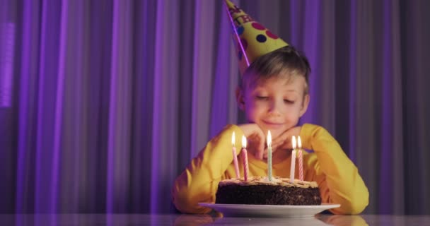かわいい男の子は誕生日にケーキの上でろうそくを吹き消す 幸せな子供はろうそくのあるケーキを見ています 子供はケーキを見て誕生日の願いを叶えます 少年は誕生日を祝う 幸福の概念 — ストック動画
