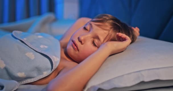 8歳の少年はカニの中で甘い眠りにつく その側に眠っている子供の顔を閉じる 真夜中に眠っている子供の追跡ショット リラックスして休んでください 4Kベッドで寝ている子供の映像 — ストック動画