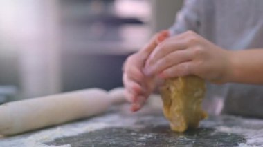 Çocuğun elleri bir parça hamur tutuyor ve sıkıyor, yakın görüş. Çocuk mutfakta yemek pişiriyor. 8 yaşındaki çocuk evde yemek pişiriyor. Yavaş çekim 4K görüntüsü. Çocuk elindeki hamuru karıştırıyor..  