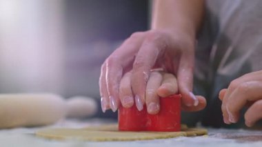 Bir anne ve çocuğun elleri hamurdan kalp yapar, yakın çekim görüntüsü. Beyaz çocuk ve annesi mutfak masasında hamurdan kalpler hazırlıyorlar. Aile evde yemek pişirir. Yavaş çekim görüntüleri 