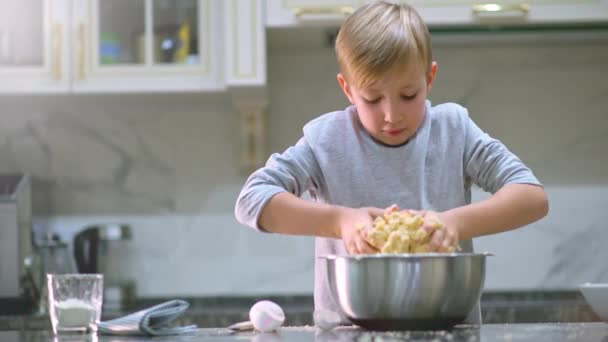 スローモーション4K映像 キッチンでの少年料理 白い少年がクッキーのために手で生地を攪拌 子供はスチールボウルにケーキのための成分を混合しています 8歳の子供が家庭で料理をする — ストック動画