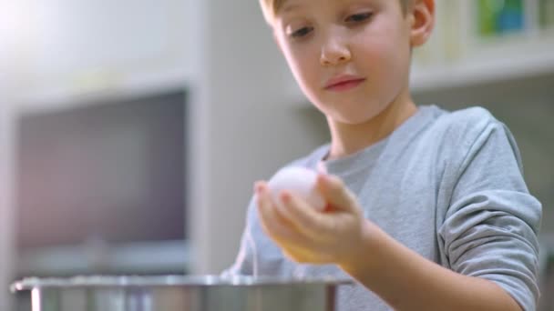 白い少年は卵を取り 生地とボウルにそれを破るし キッチンで子供料理 スチールボウルにケーキのための子供の攪拌成分 リアルタイム4K映像 — ストック動画