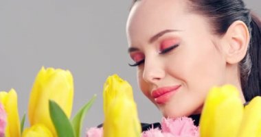Çiçekli güzel beyaz kız. Sarı lalelerden oluşan büyük buket çiçekleri olan çarpıcı esmer kız. Temiz ciltli, genç ve güzel bir kadının yakından çekilmiş yüzü. Parlak makyajlı kadın. 