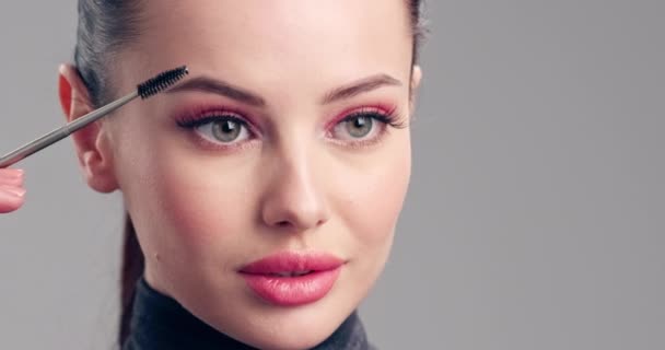 Frau macht Make-up. Die junge Frau bemalt ihre Wimpern mit einem Wimpernpinsel. Kosmetisches Konzept. Schöne brünette Modell beim Make-up. 4k Zeitlupenaufnahmen. Nahaufnahme.