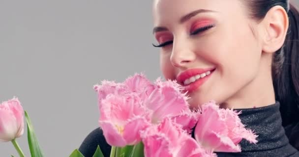 花の美しい笑顔の女の子 ピンクチューリップの大きな花束の花と幸せなブルネットの女の子 健康なきれいな肌を持つ若い美しい女性の笑顔 明るいメイクの女性 — ストック動画