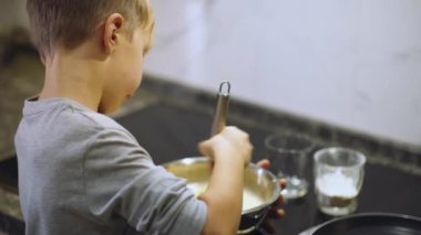 Mutfakta yemek pişiren 8 yaşında bir çocuk. Çocuk krep karışımını çırpıcıyla çırpıyor. Çocuk kurabiye yapmak için un karışımını karıştırıyor. Yemek zamanı. Çocukluk kavramı. 