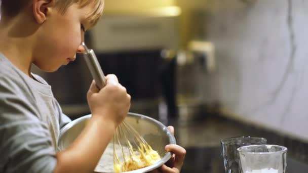 8岁的男孩在厨房里做饭 孩子们用铁碗里的威士忌搅拌着煎饼混合物 男孩把面粉混合在一起做饼干 吃饭时间 童年的概念 — 图库视频影像
